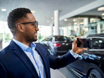 Car salesman recording a video of a new car in a showroom.